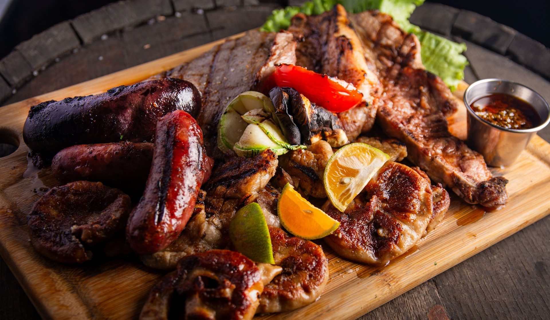 Parrillada argentina sobre tabla de barril con chorizo, morcilla y chimichurri