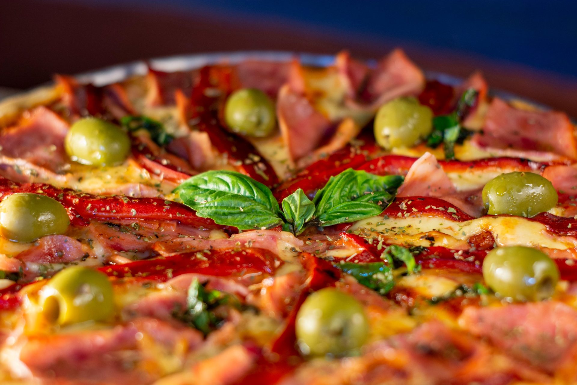 Primer plano de una pizza artesanal con aceitunas, albahaca y morrón